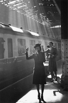 black and white photograph of woman waving at train on platform with sunbeams shining down