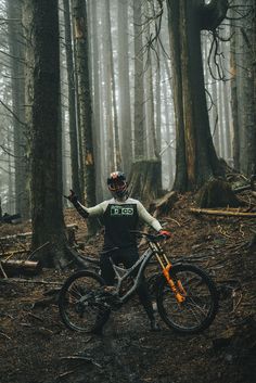 a man standing next to his bike in the middle of a forest filled with trees