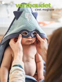 a woman holding a baby wrapped in a towel with a cat mask on it's head