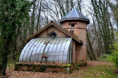 an old brick building with a metal roof in the middle of some trees and leaves