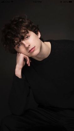 a young man with curly hair is posing for a photo in black shirt and pants