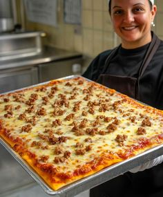 a woman holding up a pizza with meat toppings on it in a kitchen area