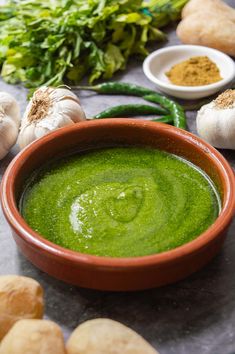 a bowl filled with green liquid surrounded by garlic and other ingredients on a table top