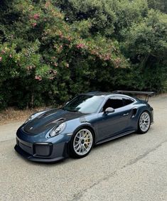 a blue sports car parked on the side of a road next to bushes and trees