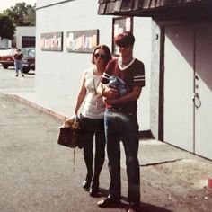 a man and woman standing in front of a building with a baby on their lap