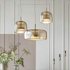 a dining room table with four lights hanging from it's ceiling and two vases filled with flowers