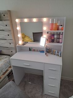 a white desk topped with a mirror and lots of lights on top of it next to a bed