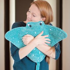 a woman is holding a blue crocheted frog pillow