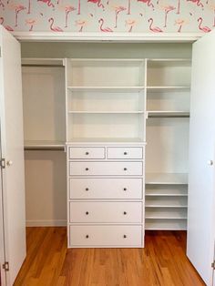 an empty closet with white drawers and pink flamingos on the wall