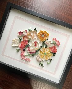 paper flowers in a black frame on a wooden table