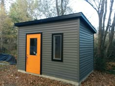 a small gray shed with an orange door in the middle of some leaves and trees