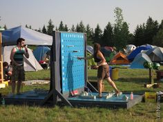 two people are standing in front of a large blue board on the grass with tents behind them