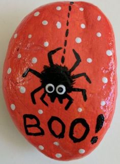 an orange painted rock with a spider on it's face and the words boo written in black