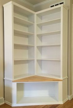 an empty bookcase in the corner of a room with wood floors and white walls