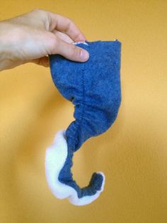 a hand holding a blue stuffed animal on top of a yellow wall next to a pair of scissors