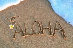 the word aloha written in sand with a flower on it