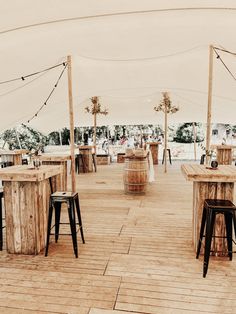 tables and stools are set up on the wooden deck under a tent with string lights