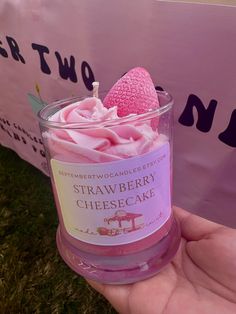 a hand holding a small glass cup filled with pink whipped cream and a strawberry on top