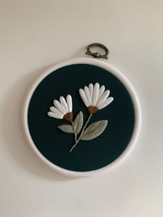 two white flowers on a black background in a circular frame with a keychain