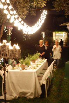 people standing around a table with lights strung from it