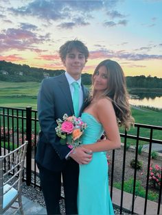 a young man and woman standing next to each other in front of a fence at sunset