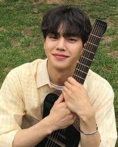 a young man holding an acoustic guitar in his hands while sitting on the grass outside