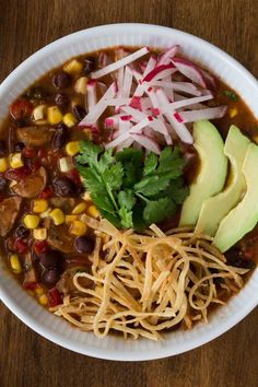 a white bowl filled with chili, beans and avocado on top of a wooden table