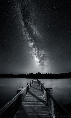 the night sky is filled with stars above a wooden dock on a body of water