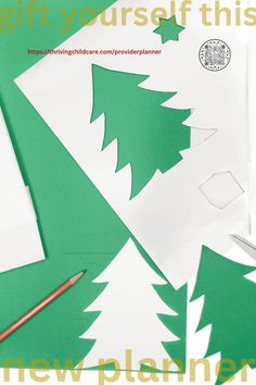 paper cut out of christmas trees on top of a table with scissors and pencils