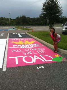 a woman standing on the side of a parking lot next to a pink road sign