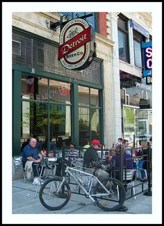 people sitting at tables in front of a restaurant with bikes parked on the side walk