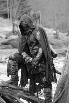 black and white photograph of a man in costume sitting on a tree stump wearing boots