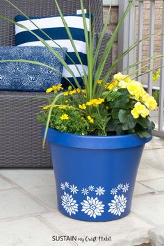 a blue flower pot with yellow flowers in it on a patio next to a wicker chair