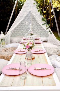 a table set up with pink plates and place settings in front of a teepee tent