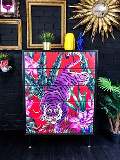 a colorful tiger painted on a dresser next to potted plants