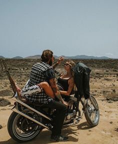 a man and woman sitting on a motorcycle in the desert