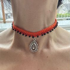 a woman wearing a red and black beaded choker with a pendant on it