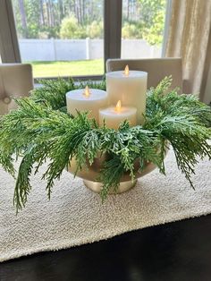 three lit candles sitting on top of a bowl filled with greenery and pine needles