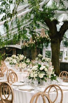 a table set up with white flowers and greenery for a wedding reception in a greenhouse