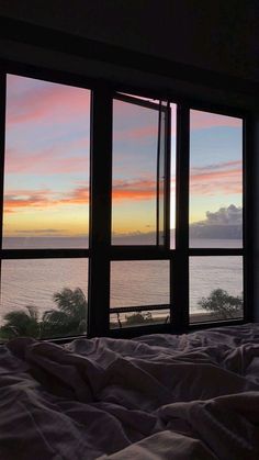 a bedroom with large windows overlooking the ocean and sunset in the distance at dusk or dawn