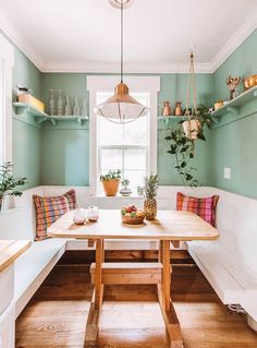 a kitchen with green walls and wooden flooring next to a window filled with potted plants