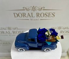 a blue truck with flowers in the back sits on top of a white cake plate