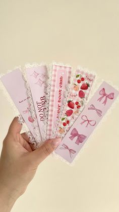 a hand holding five pink paper bookmarks with bows and strawberries on them in front of a white background