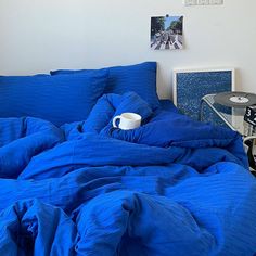 a blue comforter on top of a bed with a cup and record player next to it