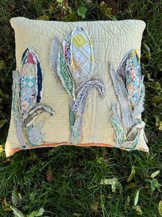 an embroidered pillow with flowers on it laying in the grass