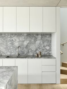 a kitchen with white cabinets and marble counter tops, along with stairs leading up to the second floor