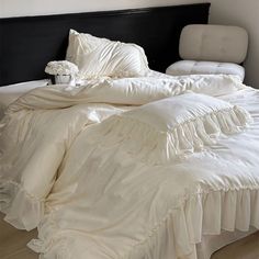 an unmade bed with white ruffles and pillows on it, in a bedroom