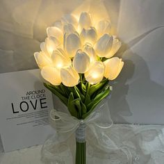 a bouquet of white tulips in a glass vase with a light on it