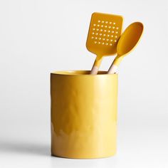 two yellow utensils in a yellow cup with holes on the sides and spoons sticking out