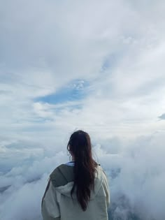 a woman standing on top of a mountain looking at the clouds